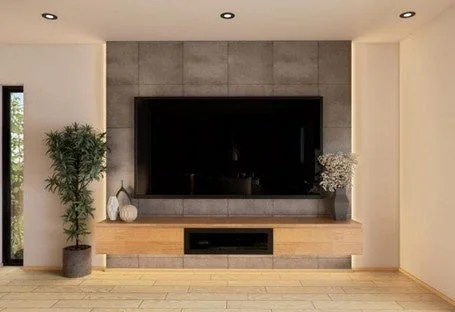 モダンなリビングルームのインテリア。コンクリート調の壁に大型テレビが設置され、木製テレビボードと観葉植物、間接照明が配された、落ち着きのある洗練された空間。