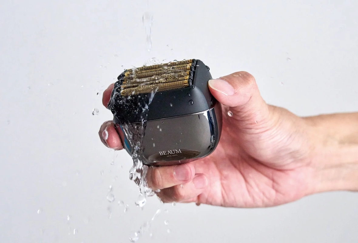 手が小型の電動シェーバーを水で洗っている様子