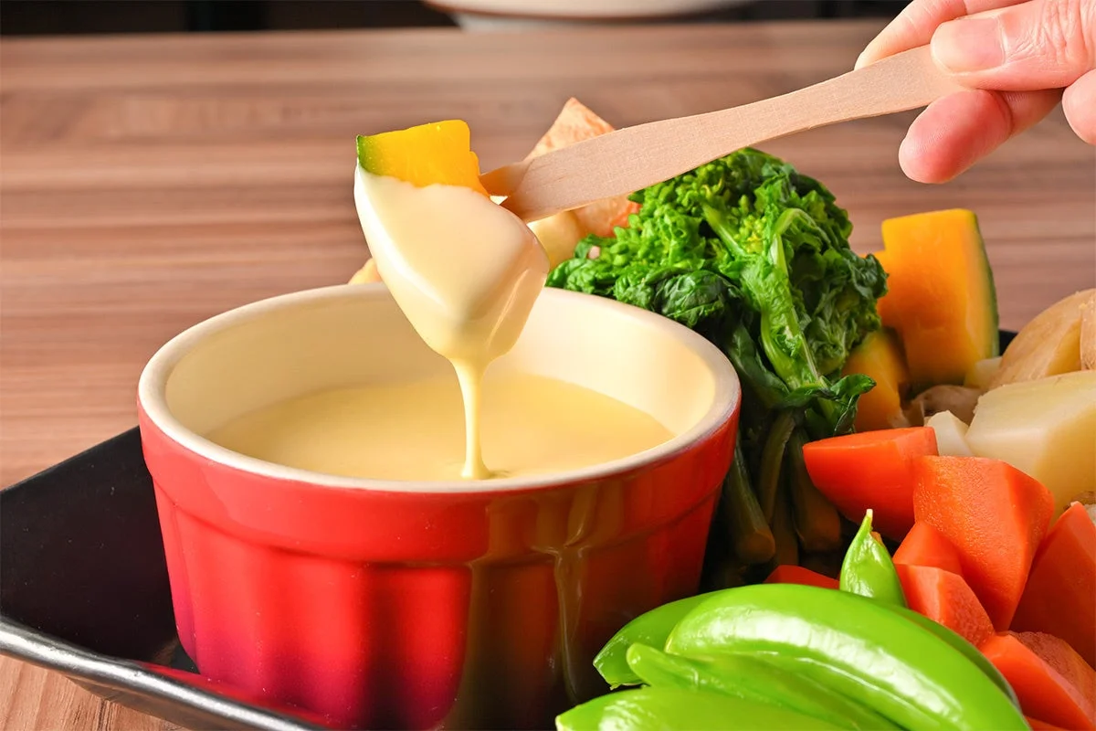 温野菜をチーズフォンデュソースにディップする様子