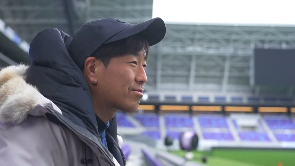 キャップと冬用ジャケットを着た男性がスタジアムで微笑む