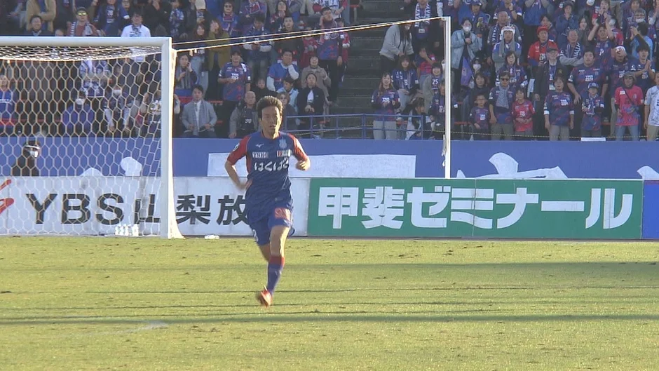 サッカーの試合中、青いユニフォームを着た選手がピッチを走る