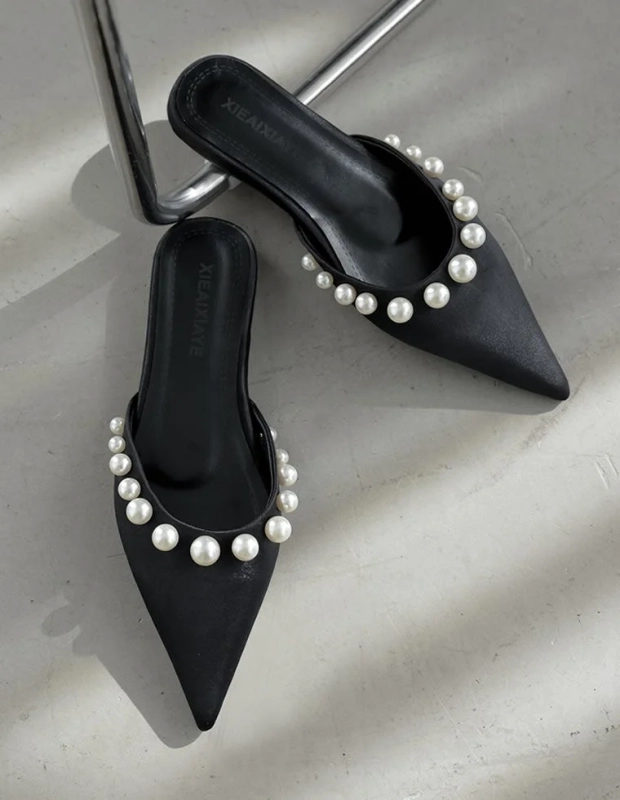 黒いポインテッドトゥのミュールが2足写っており、つま先周りに白いパールが美しく装飾されています。エレガントでフェミニンな印象のフラットシューズです。