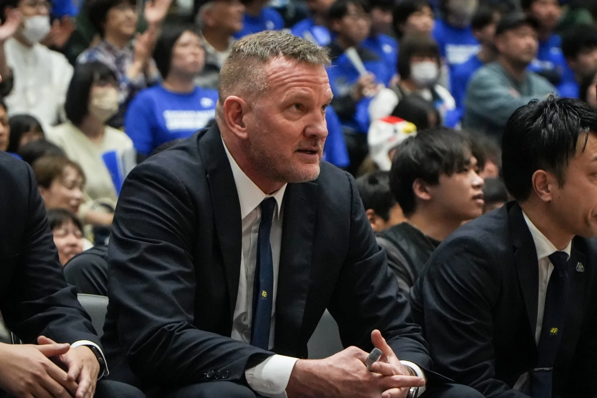 スポーツイベント会場で、スーツ姿の男性が真剣な表情で座っている